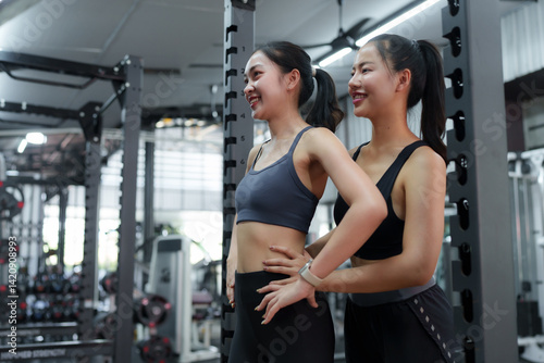 Two young women, a personal trainer and her client, are working out together in a modern gym, focusing on proper posture and technique for effective exercise