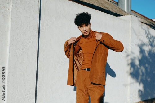 Obraz na płótnie Young man in a stylish brown outfit adjusting his jacket against a white wall w salonie