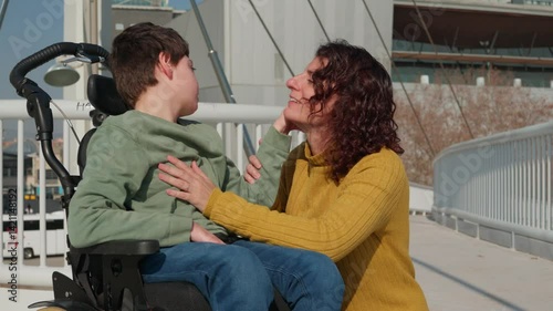 Mother comforting disabled son in wheelchair on a bridge photo