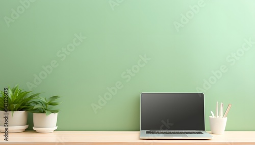 Minimalist workspace with laptop, green plants, and stationery on wooden desk against green wall