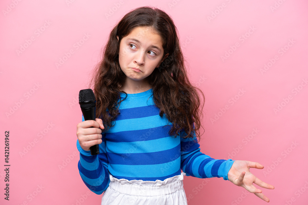 Little singer girl picking up a microphone isolated on pink background making doubts gesture while lifting the shoulders Little singer girl picking up a microphone isolated on pink background making doubts gesture while lifting the shoulders