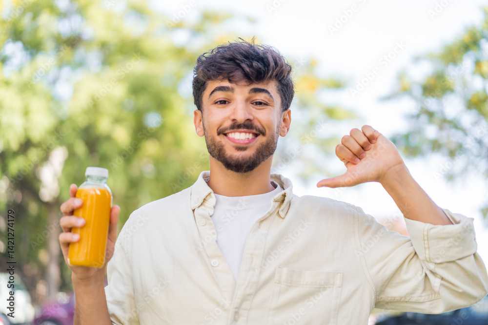 Fototapeta premium Young Arabian handsome man holding an orange juice at outdoors proud and self-satisfied