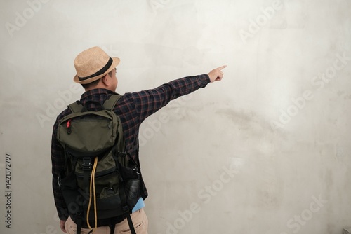 Rear view of a traveler in casual attire and hiking gear making a decisive pointing gesture, captured against a neutral backdrop