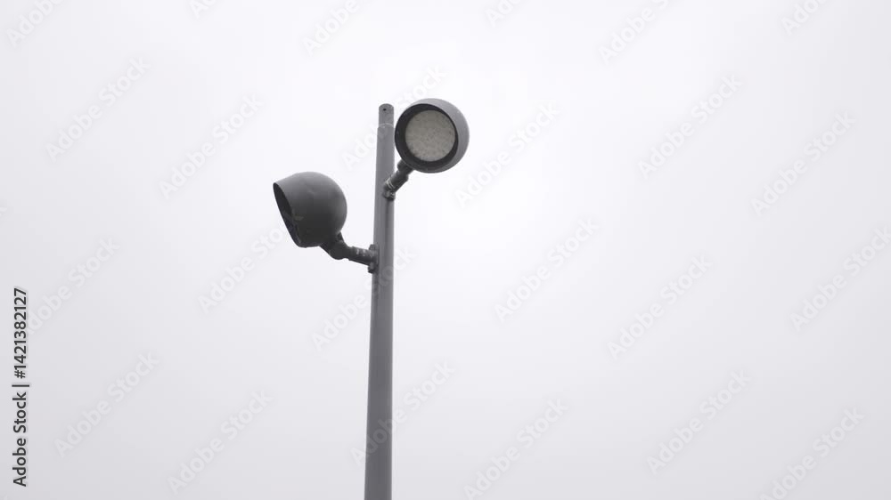 Lamppost stands still as gray sky looms above. Soon light will break through evening darkness. Sharp silhouette against dull background