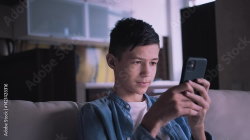 Evening Relaxation: Boy Cozying on the Couch While Using a Smartphone