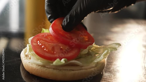 the cook's hands spread the tomato on the burger , making a hamburger or cheeseburger fast food   