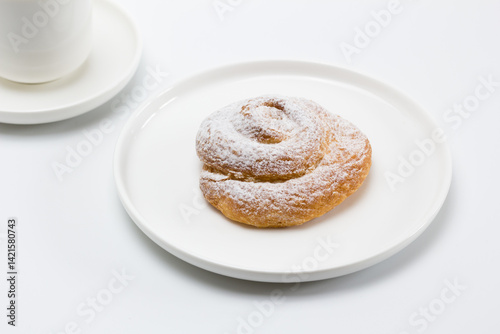 Plato con una ensaimada junto a una taza de café con leche.