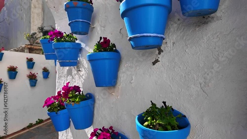Many blue flowerpots hanging on a white wall in Marbella, Spain, creating a vibrant and colorful street scene