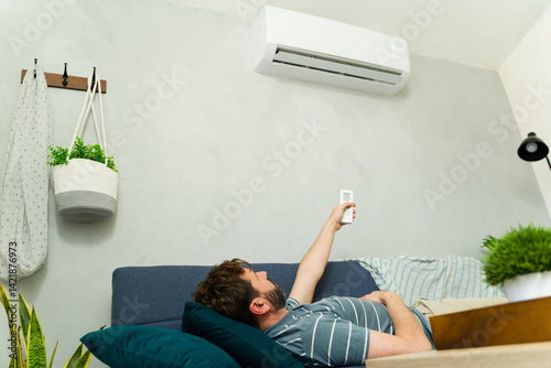 Man relaxing on sofa using remote control for air conditioning unit