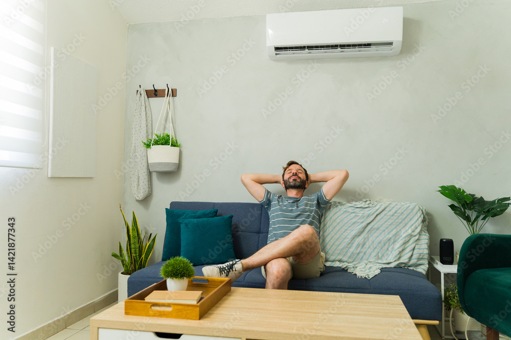Happy Caucasian man relaxing on sofa under air conditioning unit at home