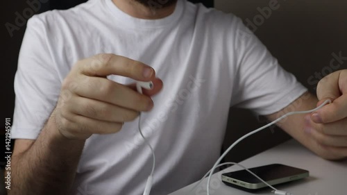 Person wearing headphones connecting earphones to smartphone while seated at a desk