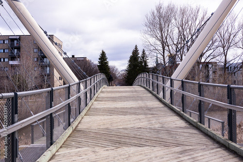 Pedestrian bridge over the Saint-Charles River in the Limoilou sector seen during a cloudy spring morning, with back view of man and dog in the background, Quebec City, Quebec, Canada