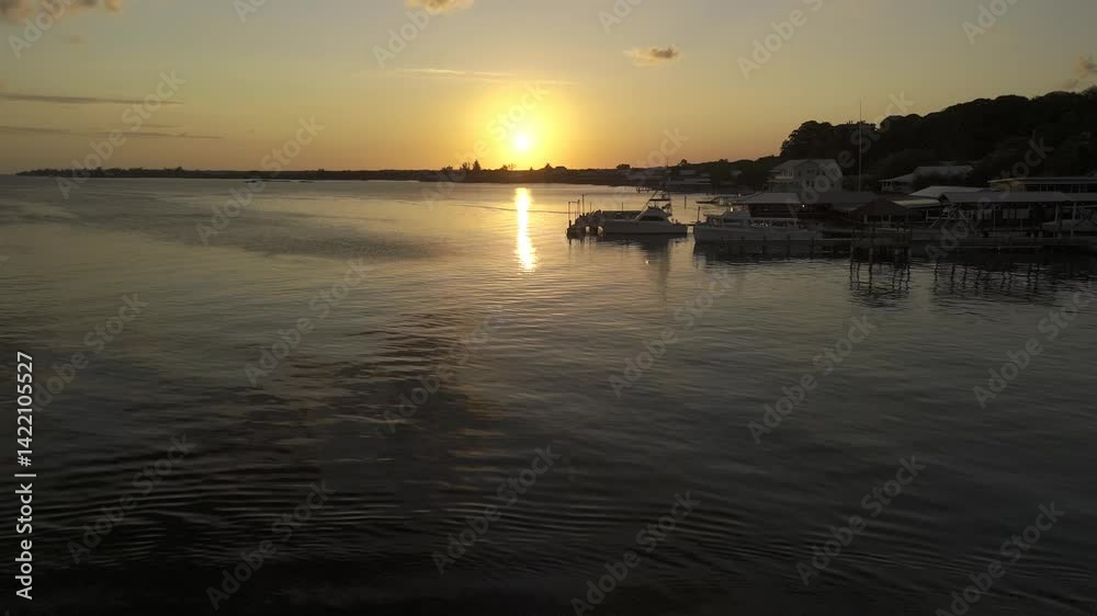 Drone flies low over water toward the sunset on a clear day as speedboat passes below