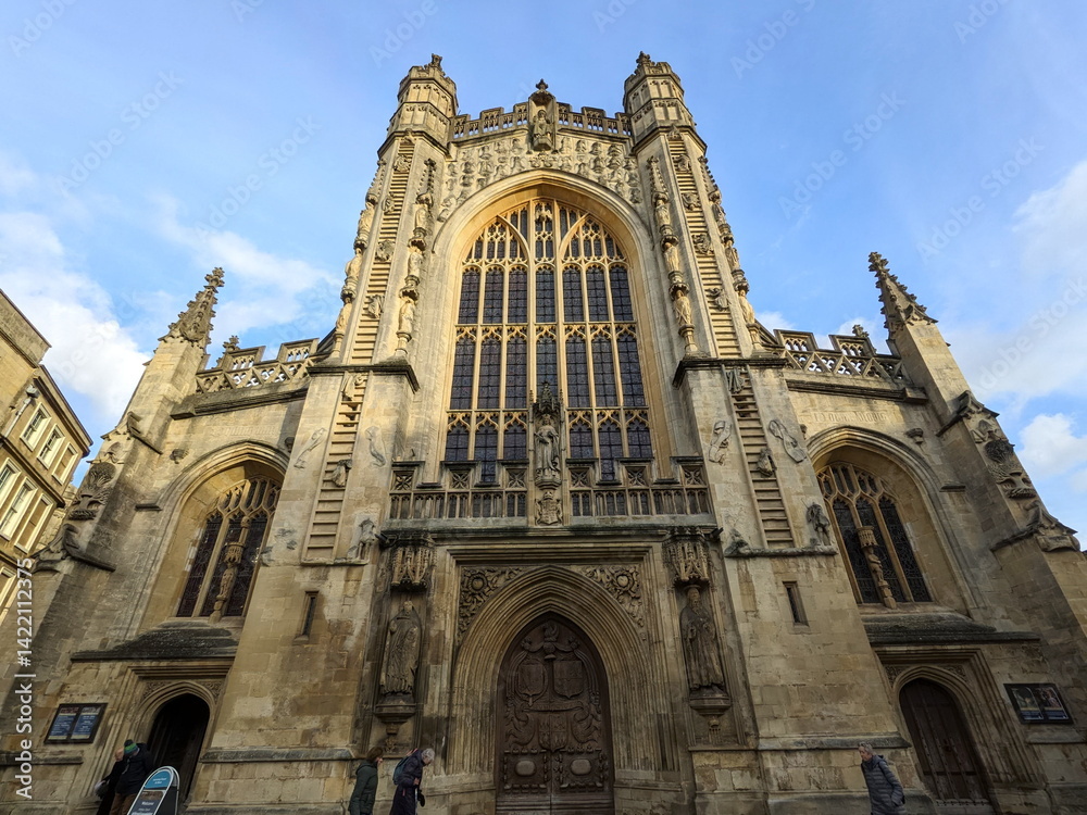 Fototapeta premium Low angle view of the intricate Gothic facade of Bath Abbey under a blue sky with clouds