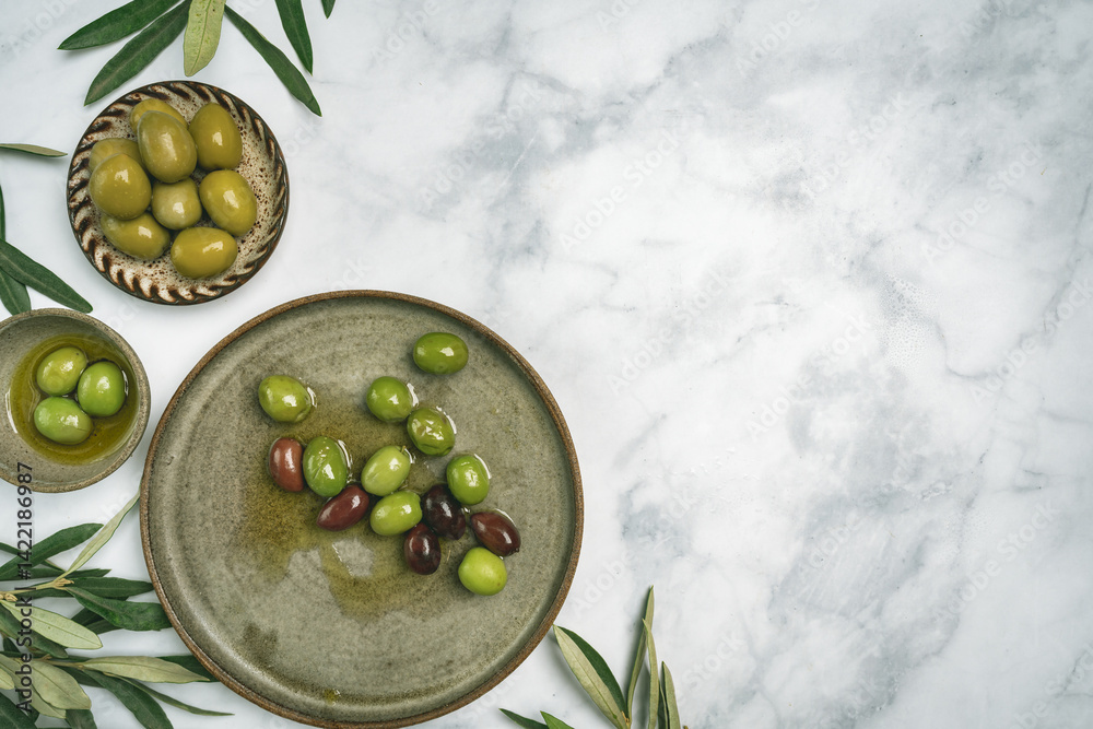 Green and black olives in a bowls and olive oil on white background top view. Olive oil and variety of green and black olives in bowls with olive leaves all around taken from above.