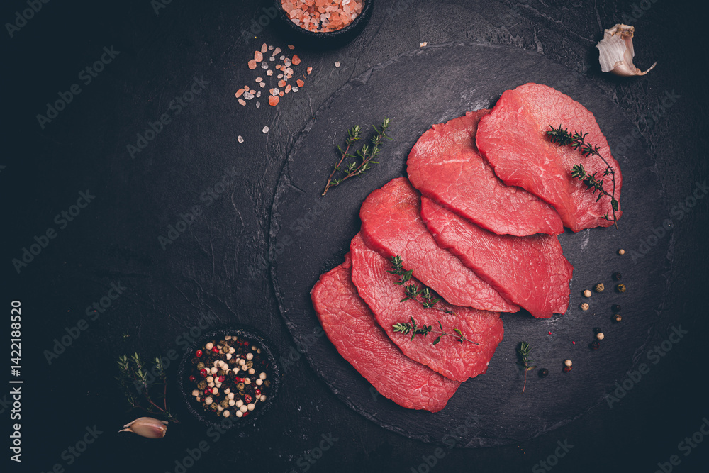 Raw sliced beef or lamb tenderloin meat, beef steaks on chopping board with spices for cooking on dark background, top view