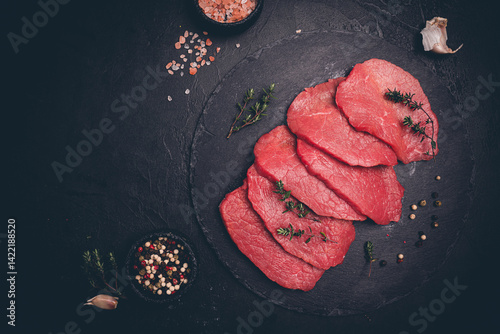 Obraz na płótnie Raw sliced beef or lamb tenderloin meat, beef steaks on chopping board with spices for cooking on dark background, top view w salonie