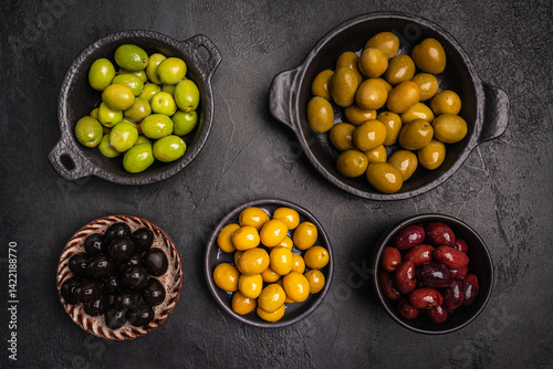 Obraz na płótnie Green and black olives in a bowls and olive oil on dark background top view. Olive oil and variety of green and black olives in bowls with olive leaves all around taken from above. w salonie
