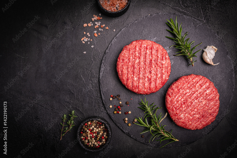 Raw steak burgers patties with ground beef and spices on a cutting board. Dark background, top view.