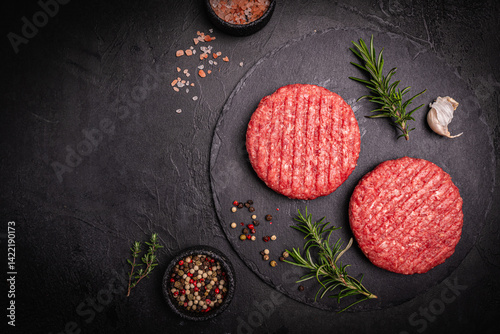 Obraz na płótnie Raw steak burgers patties with ground beef and spices on a cutting board. Dark background, top view. w salonie