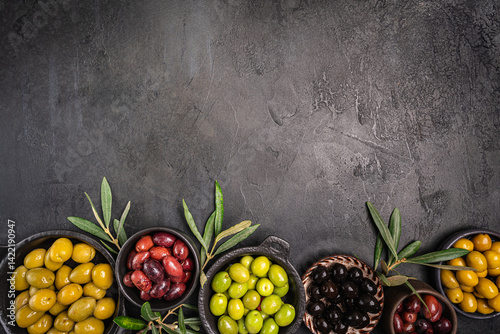 Obraz na płótnie Green and black olives in a bowls and olive oil on dark background top view. Olive oil and variety of green and black olives in bowls with olive leaves all around taken from above. w salonie
