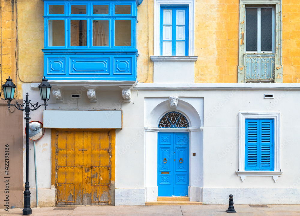Facade of a traditional Maltese building with balcony, shuttered windows and garage gate