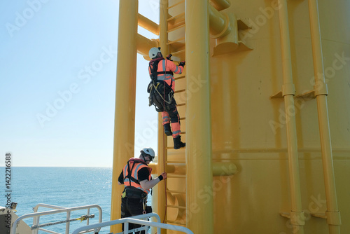 Offshore Rigger Technician Climbing Yellow Wind Turbine Monopile Ladder During Wind Farm Construction Maintenance, GWO Work On Height