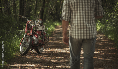 Homem a caminho da moto vintage vermelha na floresta
