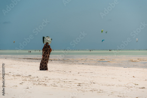 Local woman walking on paje beach in zanzibar, tanzania with kitesurfers in background