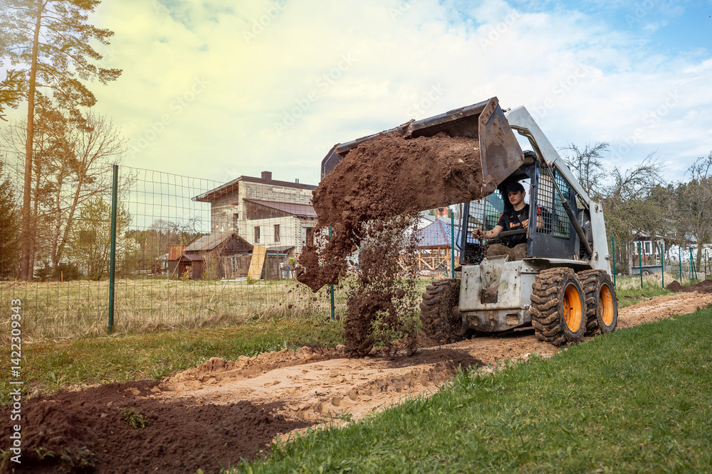 A skid steer loader with orange wheels dumps soil on a pathway near a wooden house with a slanted roof, surrounded by fields and sparse trees.