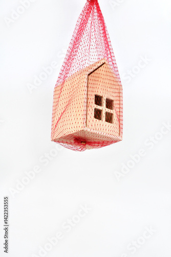 Model house suspended in a red mesh safety net. No people.  Mortgage arrears safety net concept.