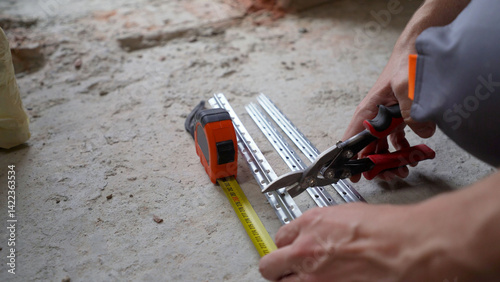 Photos Construction worker cutting metal profile using aviation snips and measuring tap