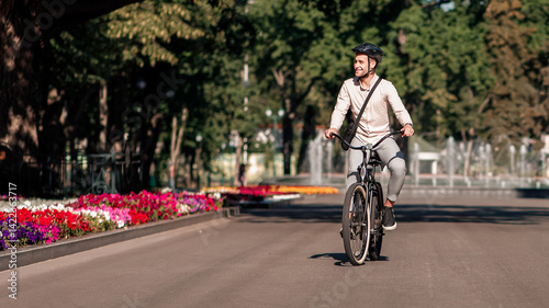 Wallpaper Mural Businessman enjoying the trip to work in morning. Happy millennial guy employee in protective helmet rides on bicycle in city in summer park, and look at landscape with fountain, outdoor, free space Torontodigital.ca