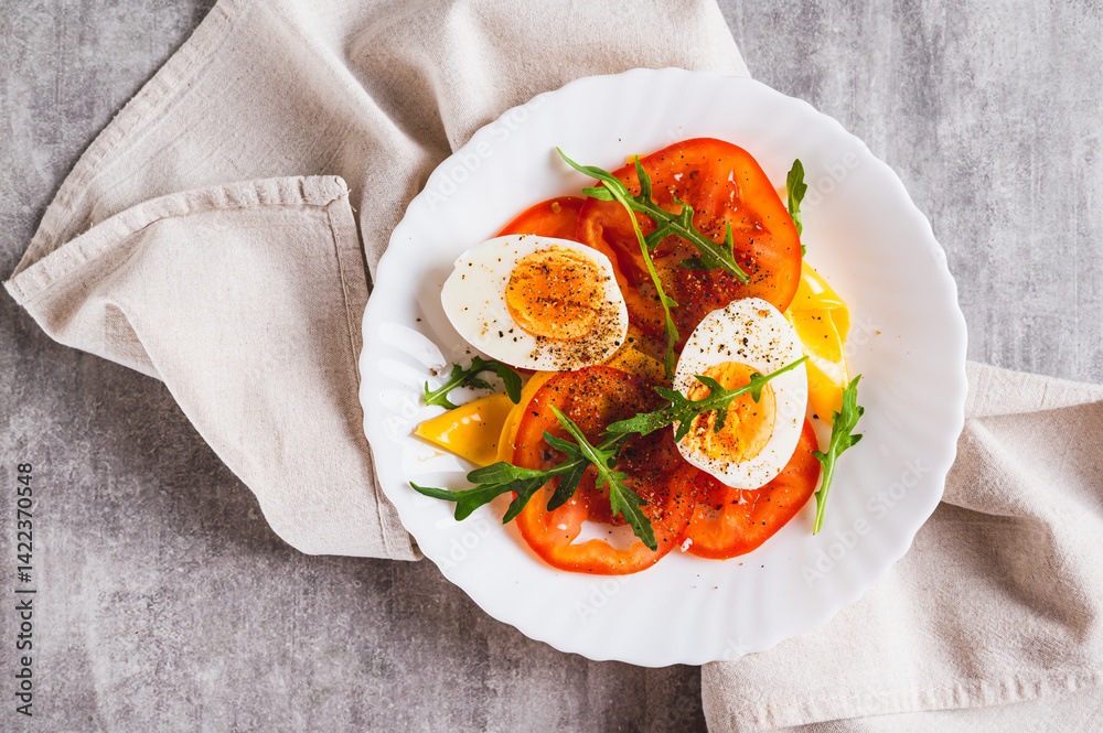 Close up of light appetizer of tomatoes, boiled egg, cheese and arugula on a plate top view