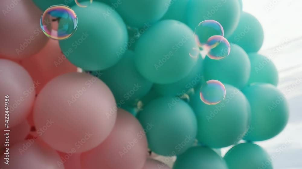 Close-up of vibrant soap bubbles floating among pastel pink and green balloons in festive atmosphere, captured with soft zoom-in and diffused sunlight

