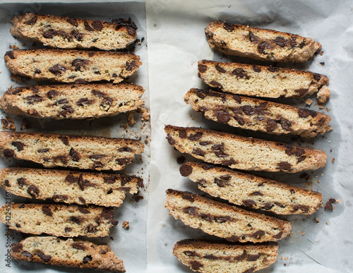 Overhead view of chocolate chip biscotti on white parchment lined tray, top view of chocolate chip cantucci cookies on a white board, flatlay of slices of biscotti cookies or twice baked cookies