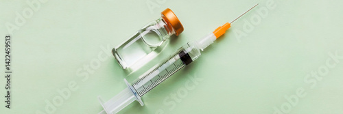 Flat lay of insulin syringe with orange cap and glass vial on pastel green background. Medical concept of diabetes treatment and control, header banner