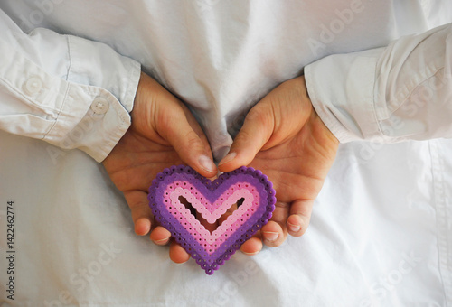 Caucasian boy's hands holding a colorful plastic heart made of ironing beads behind his back. Saint Valentine's Day, Mother's Day and Father's Day concept with copy space.