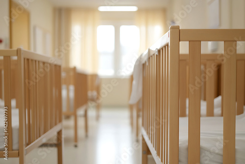 Rows of wooden cribs in a bright room, conveying a sense of stillness and anticipation of new life. Soft light through the window creates a calming atmosphere.