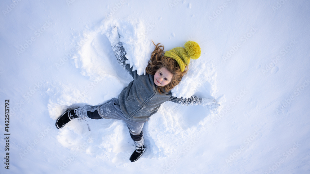 Winter fun. Child making a snow angel in winter day. Happy kid lying in the snow. Kid angel in snow. Winter kids with snowy angel wings. Smiling child on a winter day. Child in the snow lake angel.