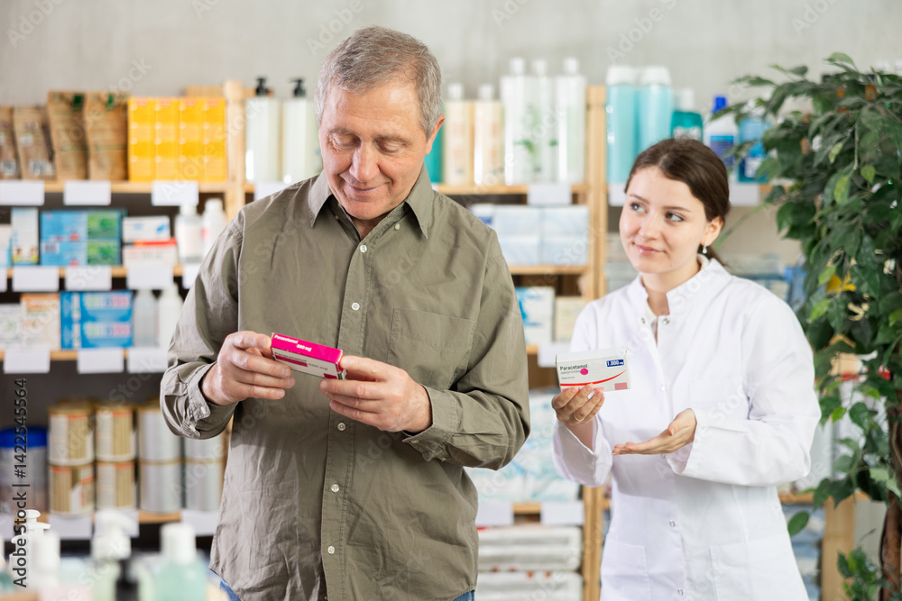 Elderly man chooses pills in modern pharmacy. Female pharmacist helps with choosing a medicine