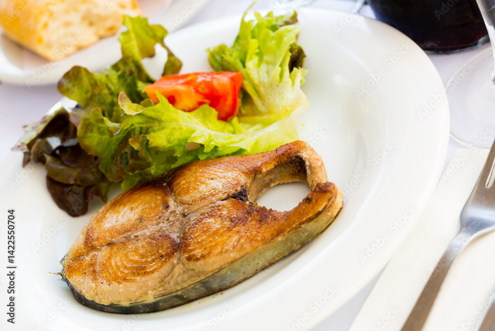 Tasty broiled steak of bonito served with vegetable salad on white plate.. Tasty broiled steak of bonito served with vegetable salad on white plate..