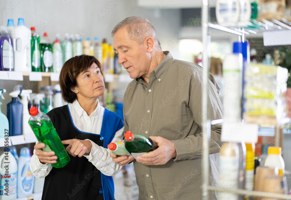 Elderly woman seller offers dishwashing detergent to elderly man buyer in household chemicals store