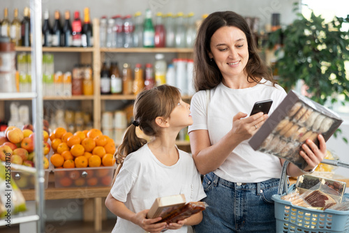 Daughter and mother choose delicious cookies in supermarket - scan QR code on label with a smartphone