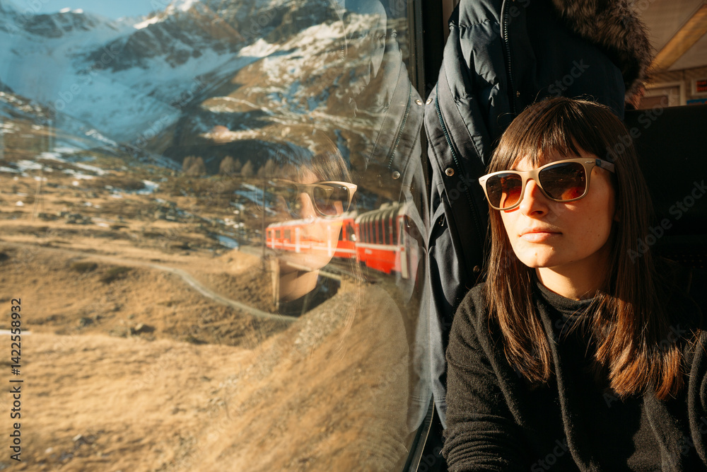 Woman in sunglasses rides a mountain train, enjoying the alpine view..