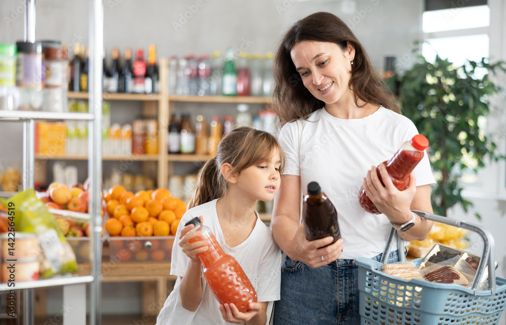 Visiting store child girl and mother purchase juice. They carefully inspect product, reflect before buying. Mom checks quality and freshness of food in store