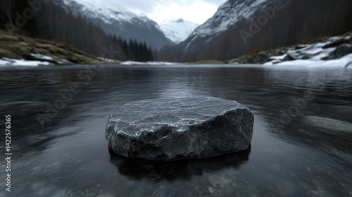 A flat dark stone pedestal stands in a calm river with snowy mountains and pine forest in the background under a cloudy sky.