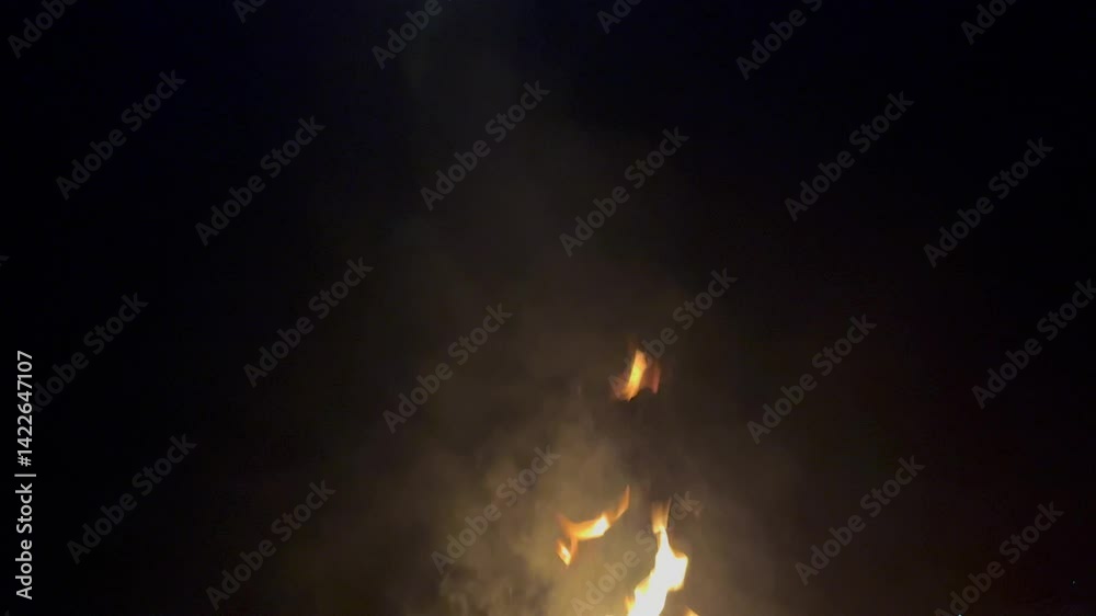 The fire burned brightly in the darkness, surrounded by smoke billowing upwards.