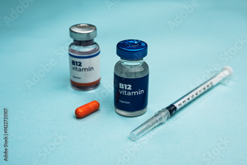 Two B12 vitamin vials and a syringe lie next to an orange capsule