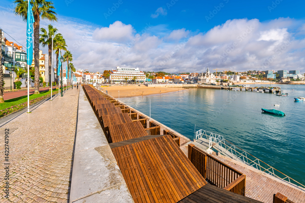 Obraz premium Avenue Dom Carlos, the waterfront tree lined street and promenade along the coast of the sandy beach and charming coastal town of Cascais, Portugal.